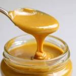 Best honey mustard recipe in a glass jar with a spoon lifting the creamy golden sauce