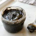 Homemade black sesame paste in open glass jar with honey drizzle on white marble surface