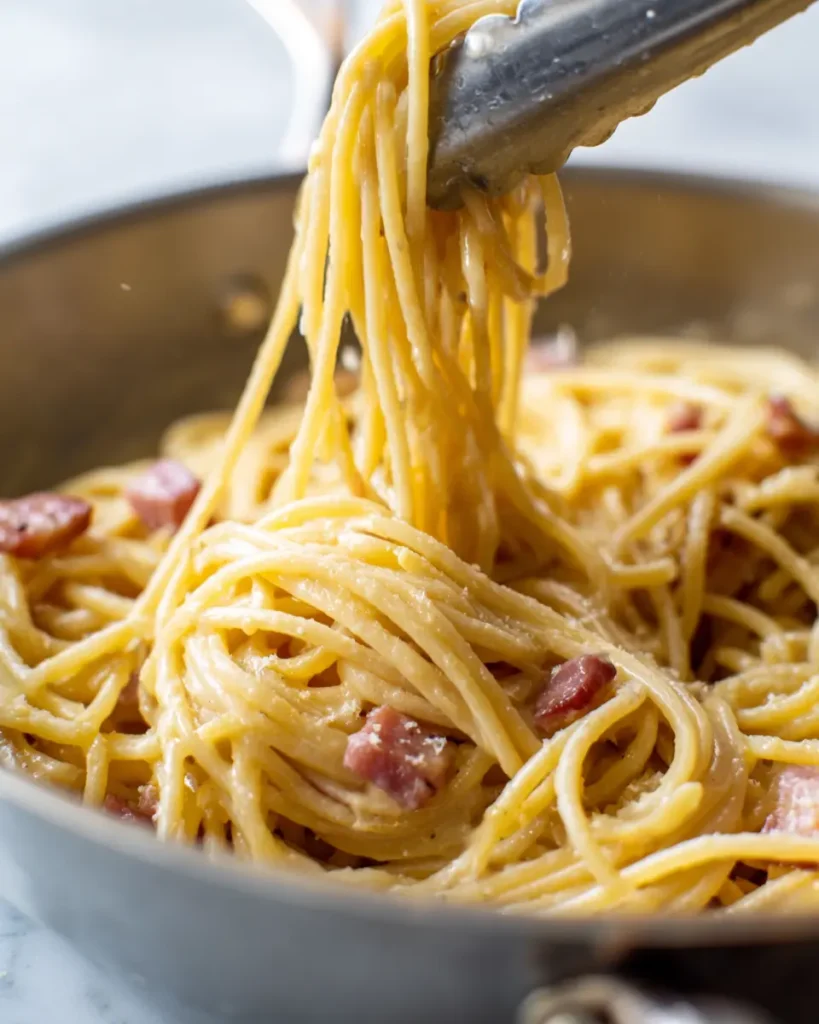 Ultimate Spaghetti Carbonara Recipe (Creamy, No Cream) 15 Spaghetti carbonara being tossed in a skillet off the heat as the silky egg sauce forms and coats every strand of pasta.