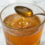 Honey and baking soda trick drink in a clear glass with golden honey drizzle