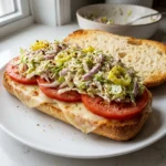 Assembling grinder sandwich recipe with salad piled high over melted cheese and tomatoes