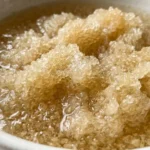 Organic gelatin powder blooming in cold water in a white ceramic bowl, close-up shot showing the texture and natural color.